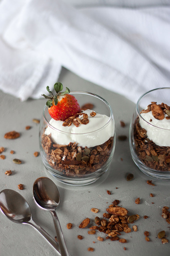 glass pot of chocolate granola topped with yogurt and berries