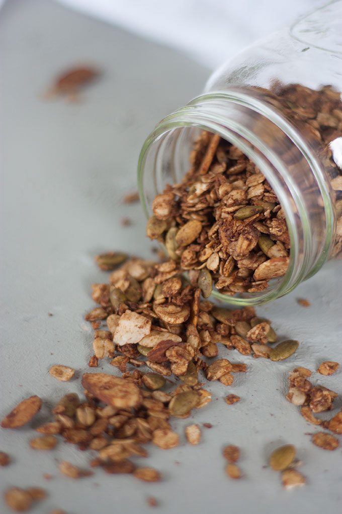 glass jar of chocolate granola on side, granola spilling out on to board