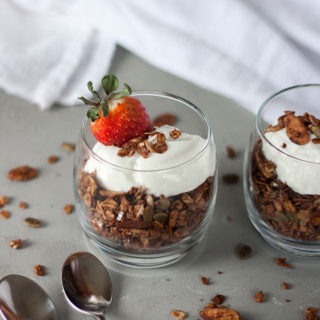 one glass pot of chocolate granola topped with yogurt and strawberries