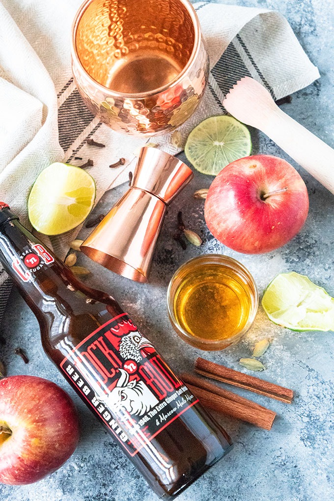 apple cider moscow mule ingredients on board - ginger beer, apples, cinnamon sticks, lime and simple syrup