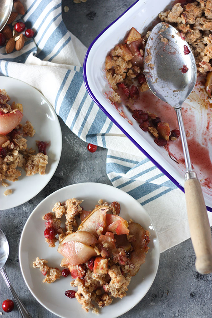 white plate of apple and pear crisp on grey background, next to white and blue enamel baking dish with crisp