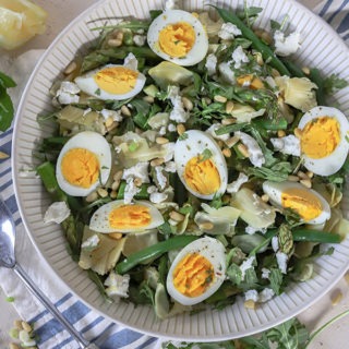 large salad bowl with aritchoke salad on a cream board with blue napkin