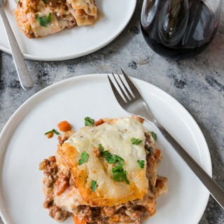 beef lasagne on a white plate next to glass of red wine