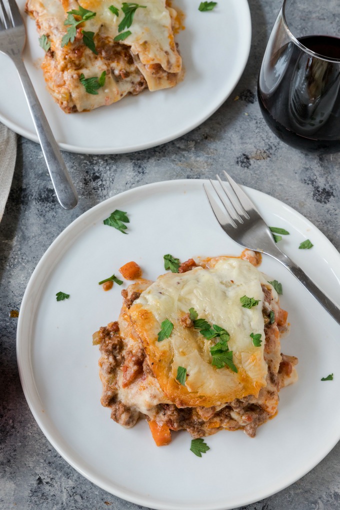 piece of beef lasagne on white plate next to glass of red wine