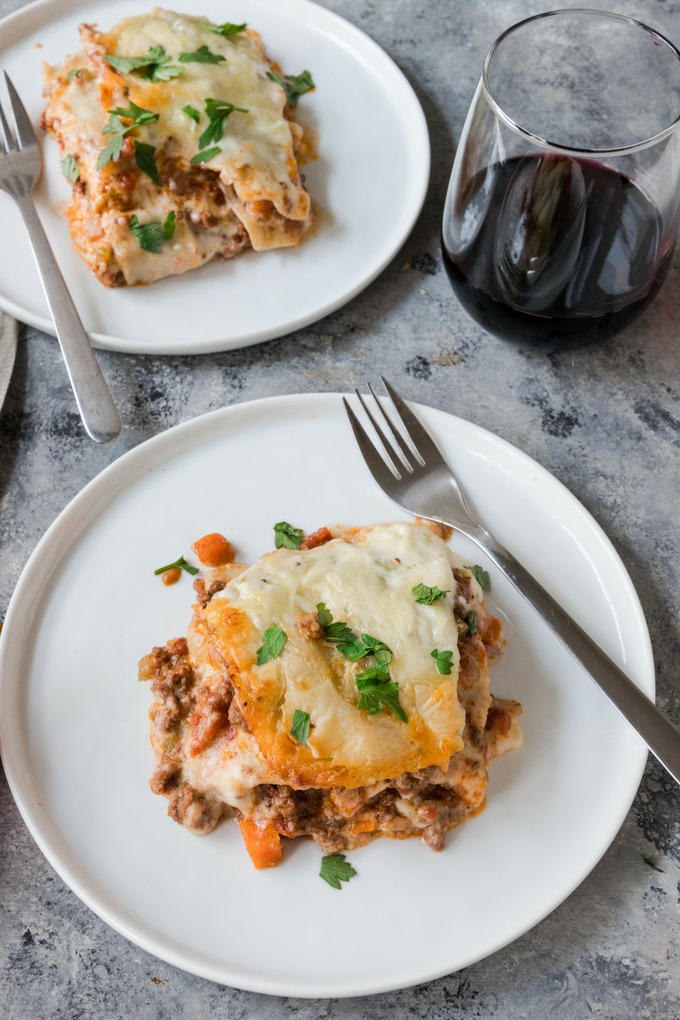 two plates of beef lasagne next to red wine glass