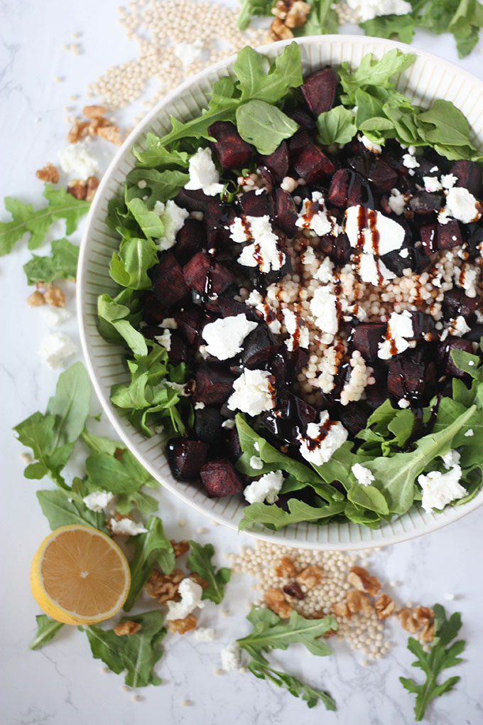 beetroot goat cheese salad in salad bowl or marble board. bowl surrounded by couscous, walnuts and arugula