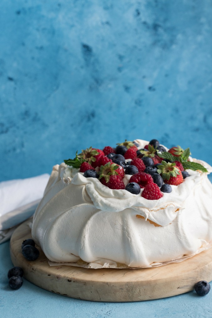 pavlova on antique wooden board covered in fresh cream and berries