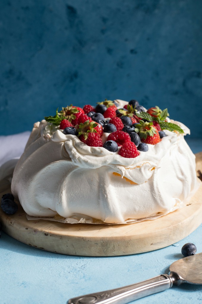 pavlova topped with fresh berries and cream on a wooden round antique board on blue background