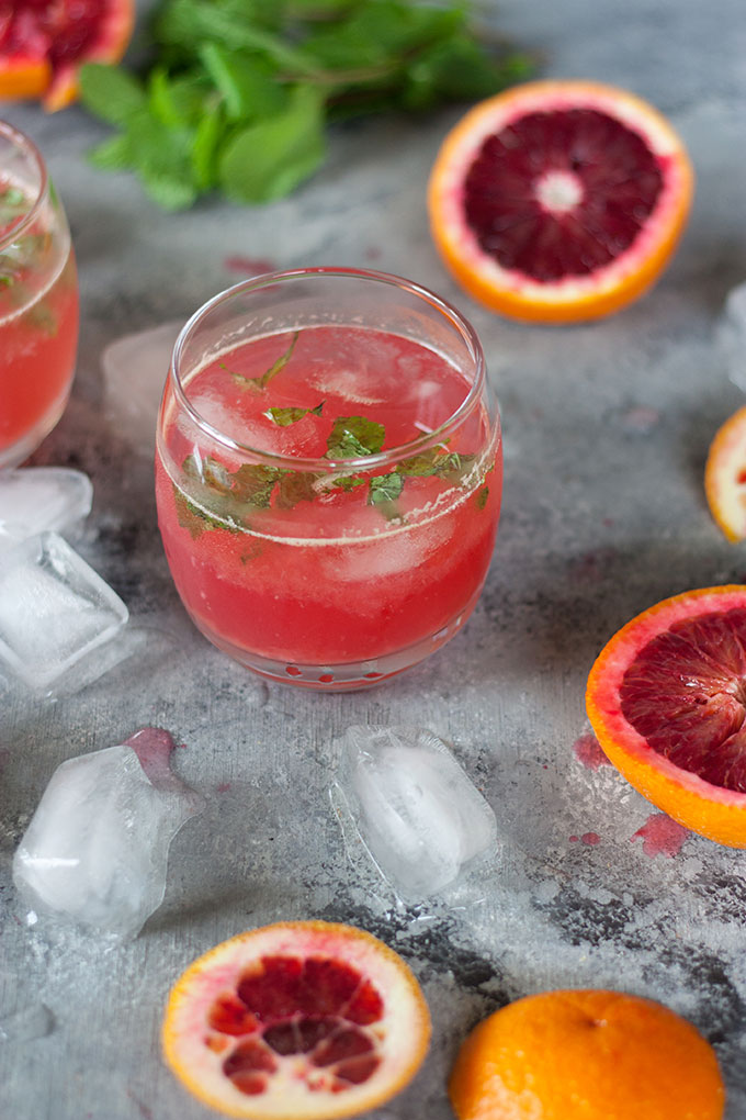 single tumbler, surrounded by blood oranges and ice cubes