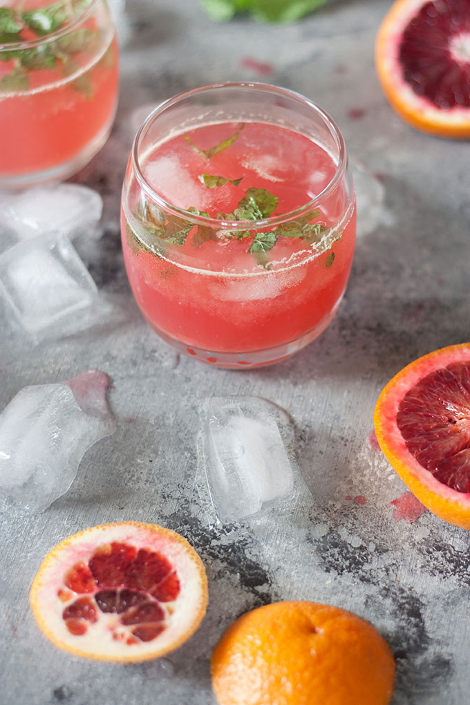 one single blood orange cocktail in small tumbler, blood orange segments on right