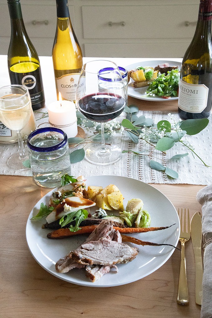 lamb and sides on plate set onto table with wines