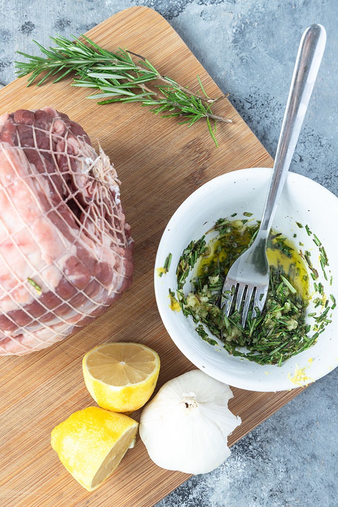 boneless lamb roast ingredients on board - lamb, lemon, garlic, rosemary and olive oil