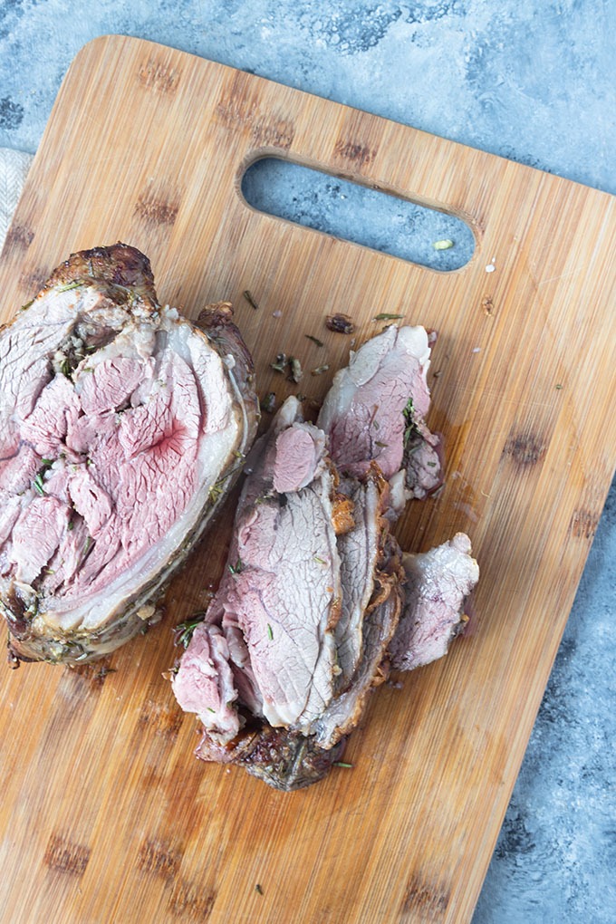 cooked and sliced boneless lamb roast on wooden board