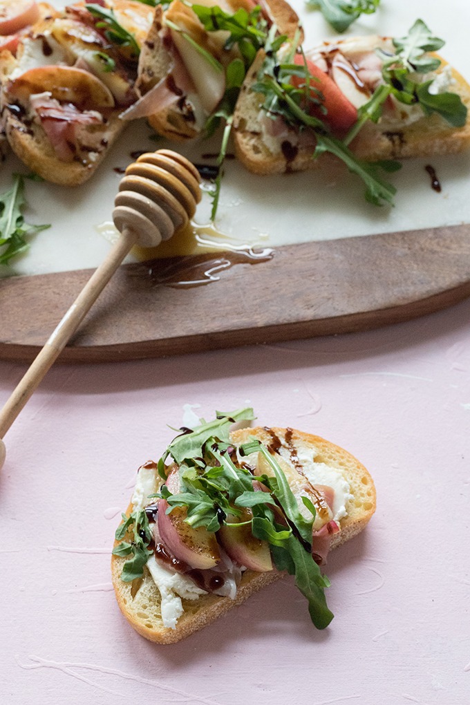 one slice of bruschetta with prosciutto, nectarine and goat cheese in front of marble board, on pink backdrop