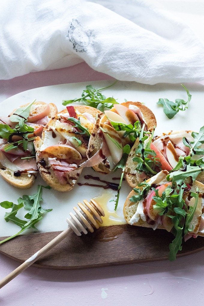 four slices of bruschetta laid out in curved pattern on marble and wooden board with white napkin and wooden honey stick