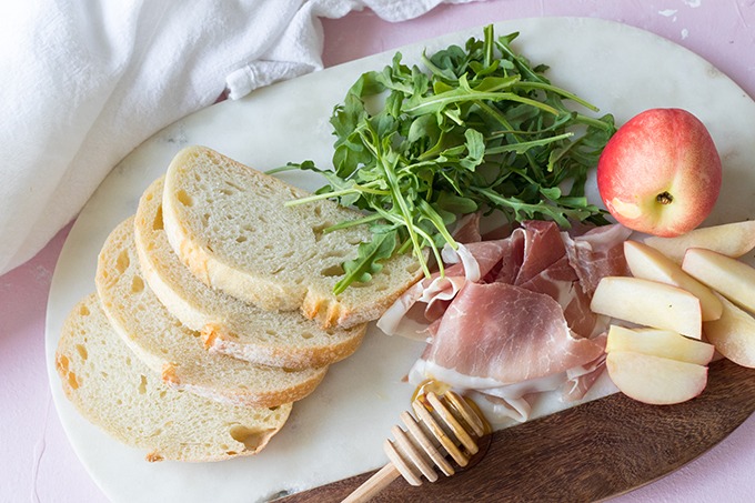 bruschetta with prosciutto ingredients on marble board, from left ot right - bread, argula, nectarine, proscuitto and honey