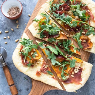 butternut squash pizza on a wooden board next to pizza cutter and salt dish