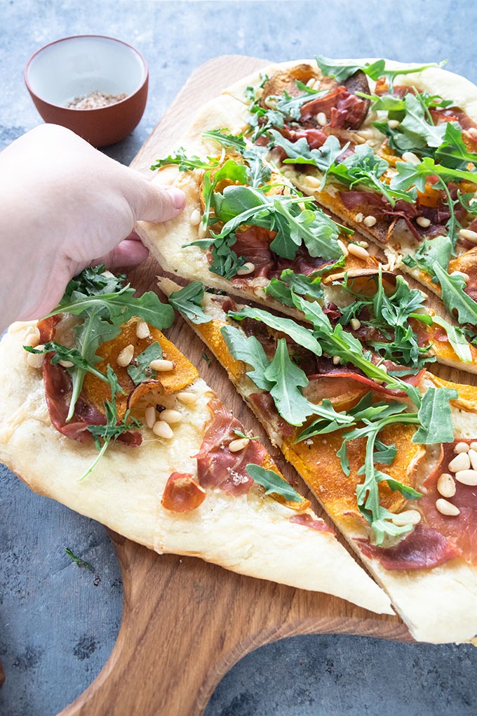 hand reaching out to grab a slice of butternut squash pizza