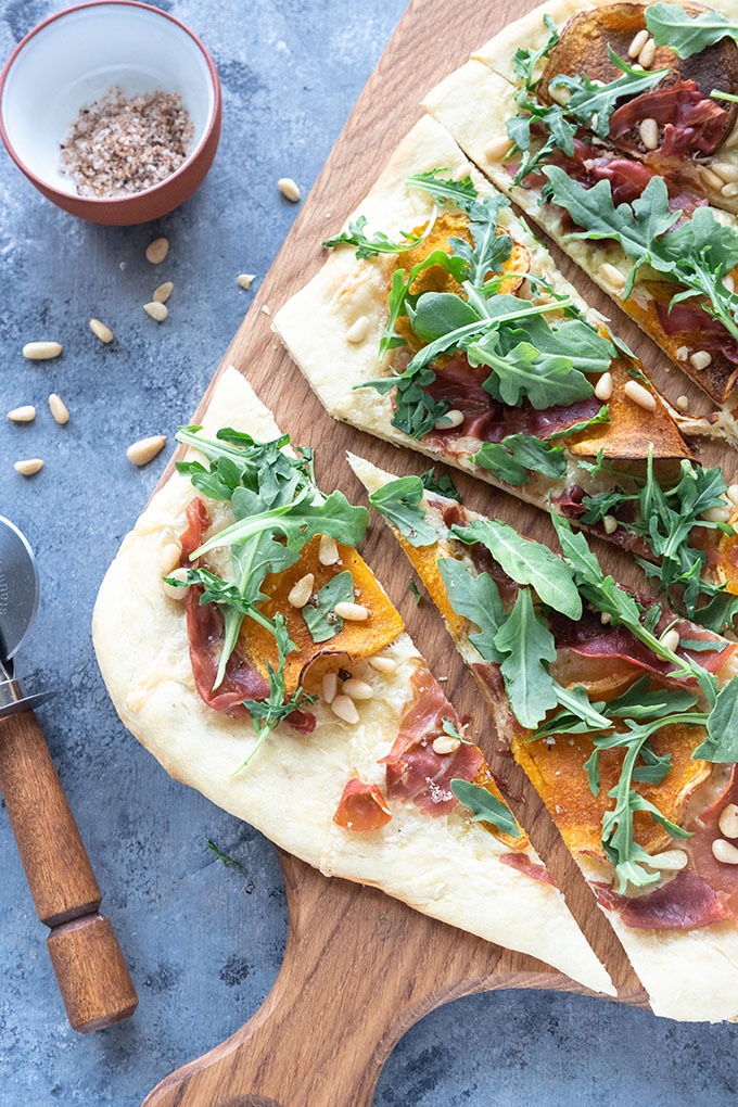 cut butternut squash pizza on wooden board with antique pizza cutter and salt pot