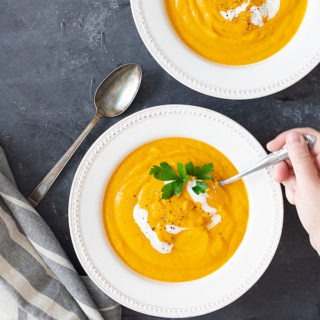 hand reaching out with a spoon to dip into carrot ginger soup