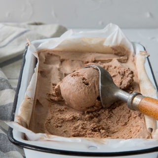 old wooden ice cream scoop, laying on chili chocolate ice cream in white enamel tin