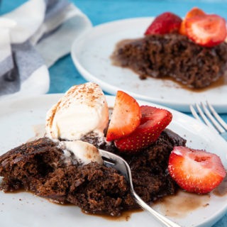 chocolate self saucing pudding on white plate with fork and strawberries