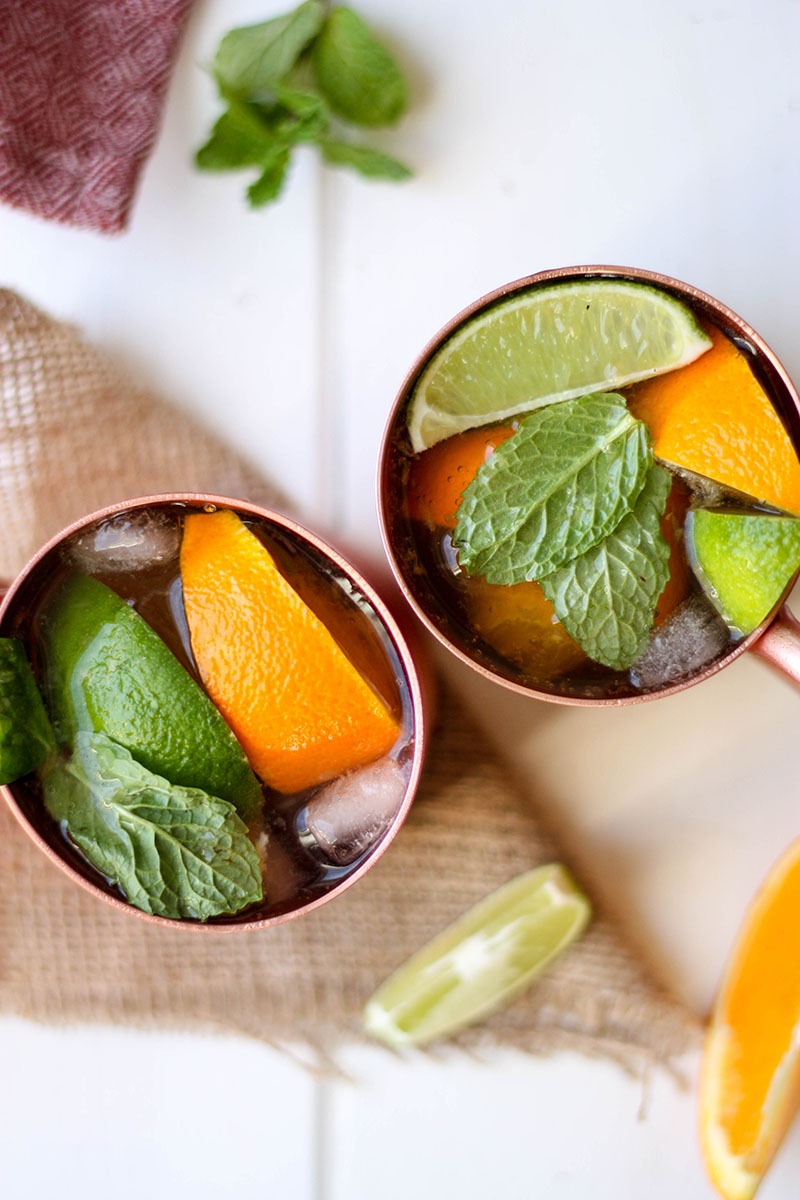 overhead of two citrus ginger dark and stormy cocktail in copper mugs on hessian square