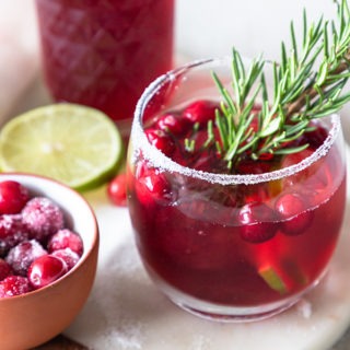 cranberry margarita in a small glass with cranberry juice in background