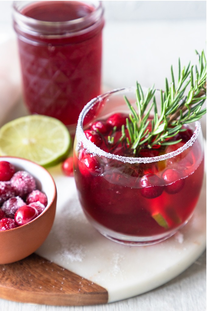 cranberry margarita in glass with cranberry juice and lime wedges