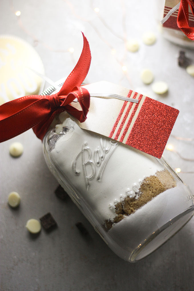 mason jar with red bow filled with ingredients for jar cookies on grey board with christmas lights