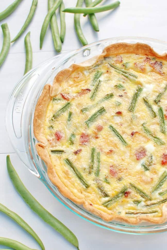 green bean quiche in glass dish, single green beans on board