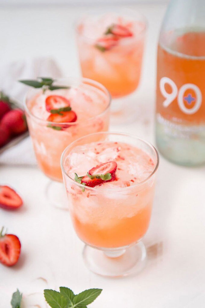 two strawberry wine cocktails on a white board in front of a bottle of wine