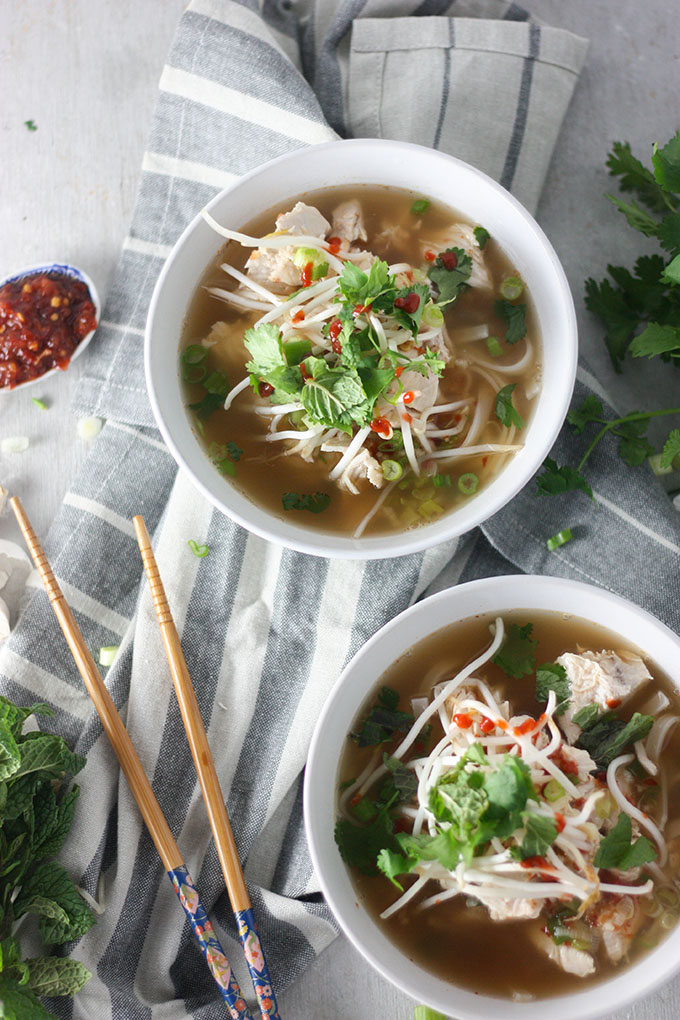 two bowls of chicken pho on grey napkin, side spoon of chili and chopsticks