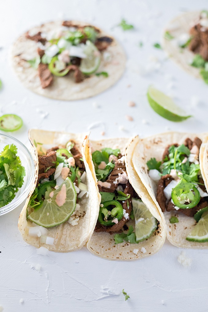 three tacos lined up next to small bowl of cilantro, single flat taco in background