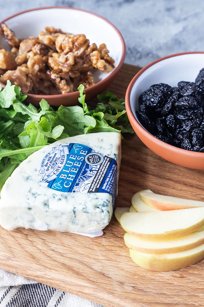 fall harvest salad recipe ingredients - candied walnuts, arugula, blue cheese, cherries and apple on wooden board