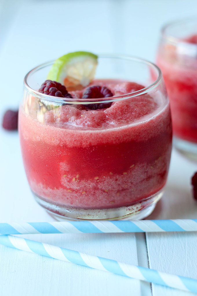 short tumbler filled with raspberry margarita concoction, behind two blue stripey straws