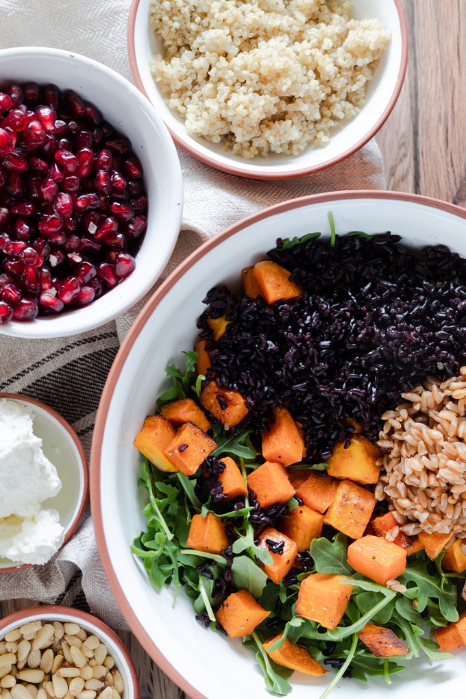 grains, pumpkin and arugula in bowl, with quinoa and pomegranate around side of bowl