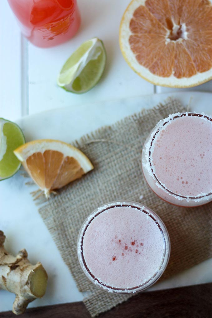 two grapefruit margaritas in glasses on hessian cloth, and marble board. 