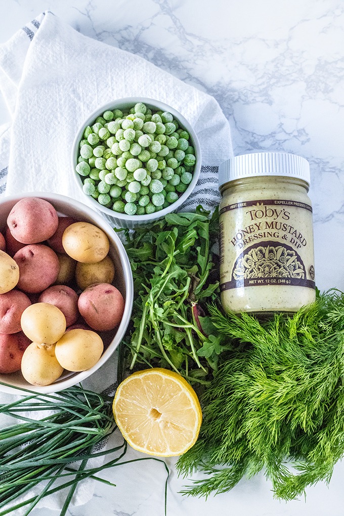 honey mustard potato salad ingredients from left to right: potatoes, peas, dressing, dill, arugula, lemon, chives