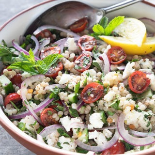 israeli couscous salad in white terra-cotta bowl with antique spoon