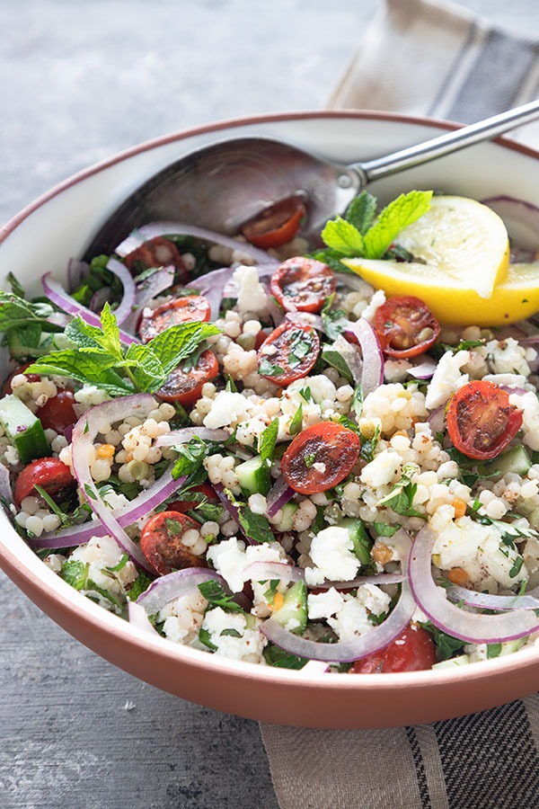 israeli couscous salad in white terra-cotta bowl with antique spoon