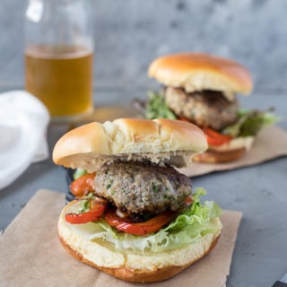 two lamb burgers with feta on brown parchment paper, in front of glass of beer