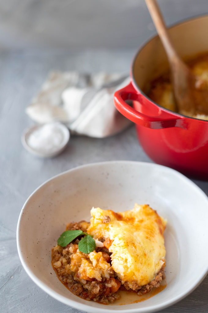 lamb shepherd's pie in a white bowl in front of red dutch oven