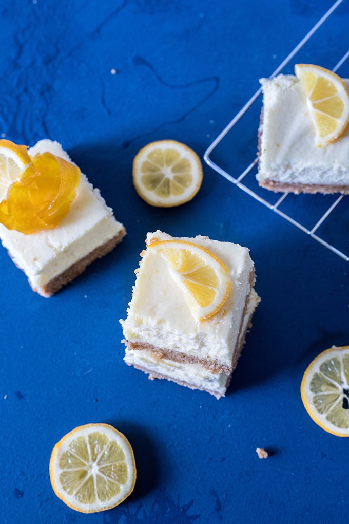 three pieces of lemon cheesecake bars on a board, three pieces of lemon slices and wire rack