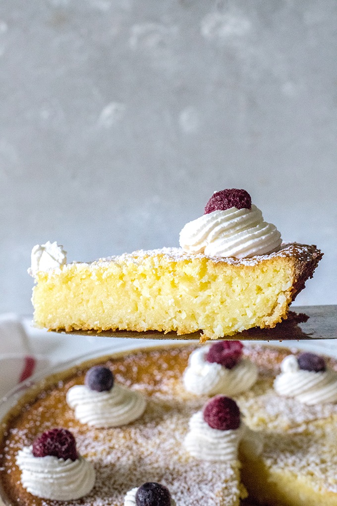 slice of lemon coconut tart being held up above remaining tart