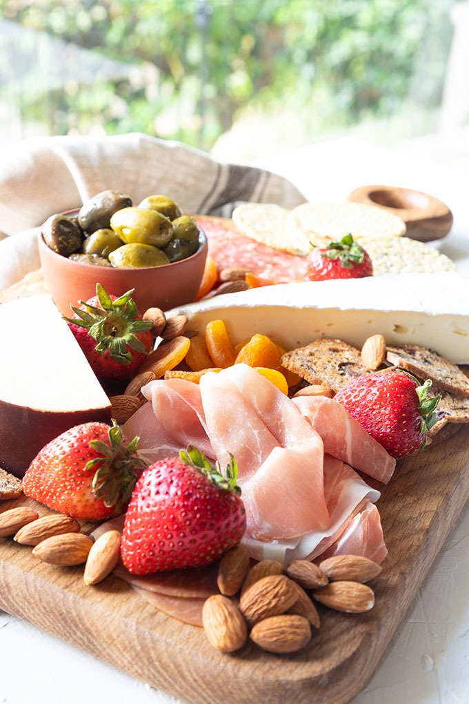 meat and cheese board in front of window with green bushes in background