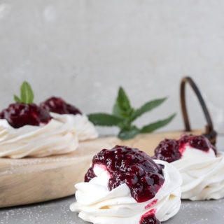 one vanilla meringue topped with blackberry sauce on a grey board, round antique board with other meringues in background