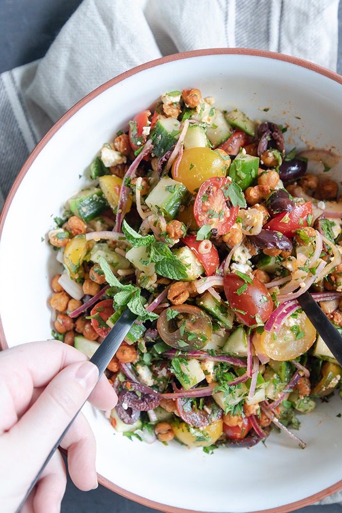 hands using utensils to toss moroccan chickpea salad