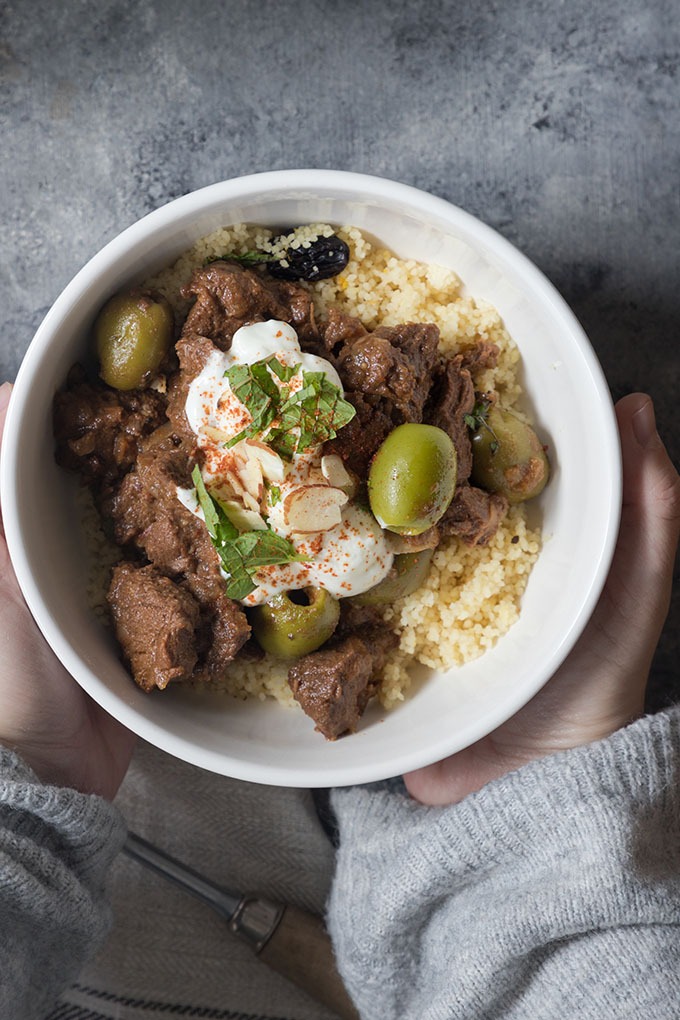 hands holding a bowl of moroccan lamb tagine with couscous