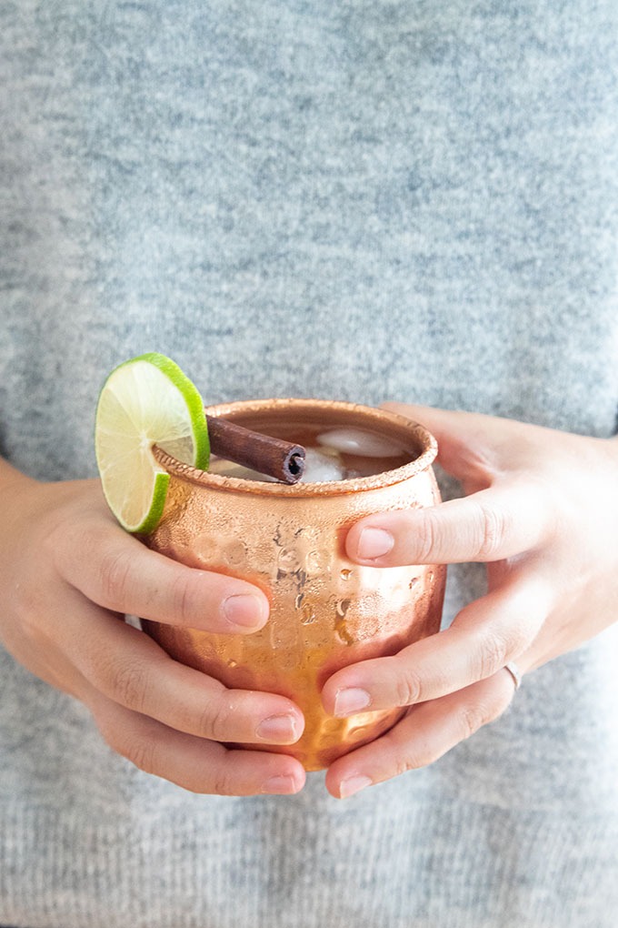 hand holding copper mug of apple cider moscow mule in front of grey sweater